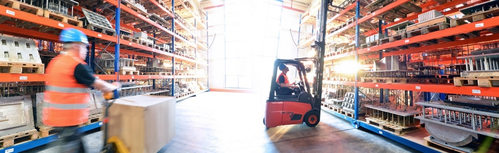 Logistik im Warenlager – Arbeiter mit Hubwagen und Gabelstapler am Hochregal // Logistics in warehouse – Worker with pallet truck and forklift truck on high rack